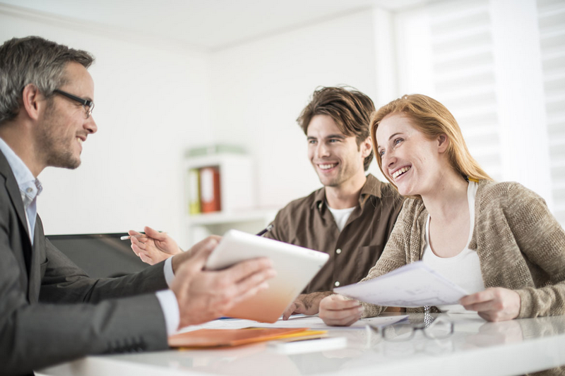 Three people sit around a table, smiling and discussing, with documents and a tablet in hand.